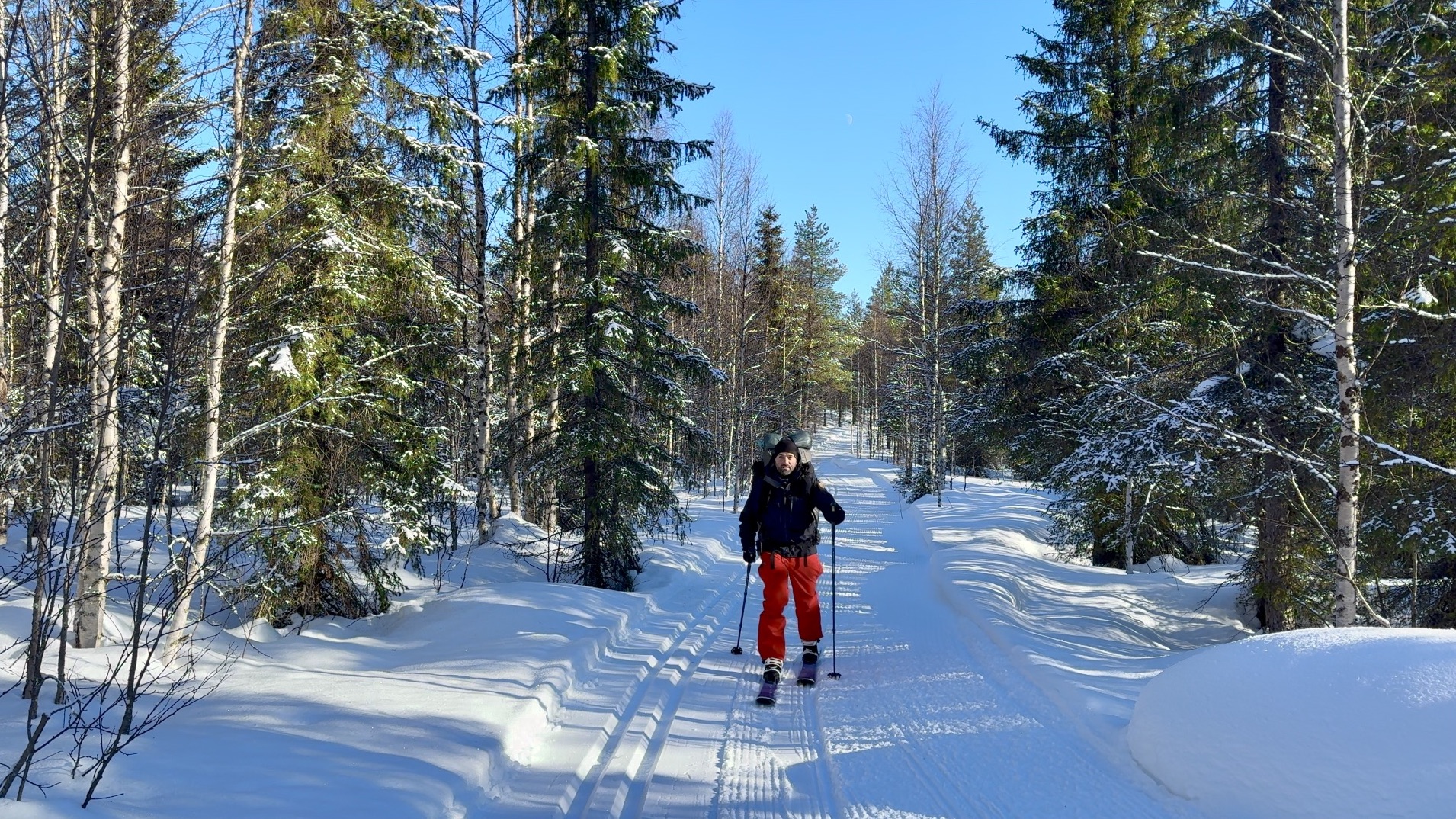 Photography of a boreal forest in Lapland with a ski trail and me skiing it with a heavy backpack