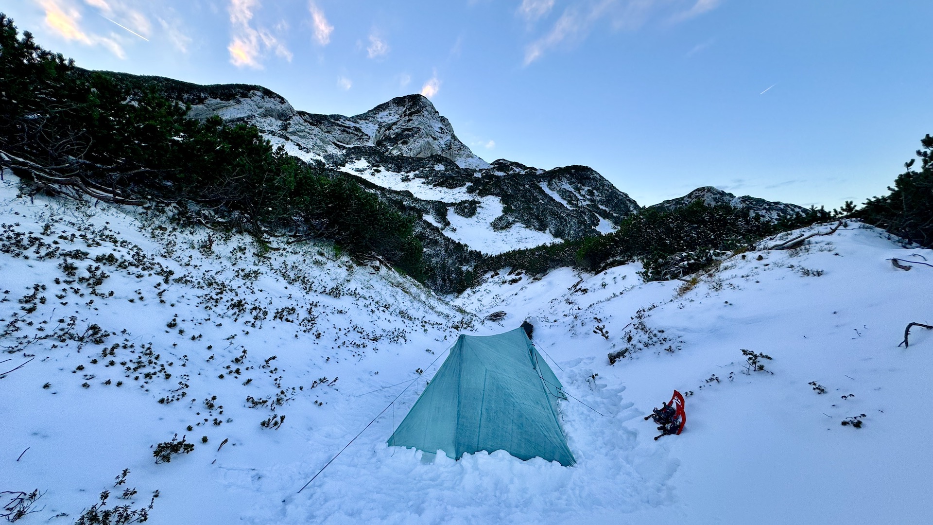 Photography of an high-tech tent setup in the snow at the foot of a snow-covered mountain with snow-shoes planted in the snow